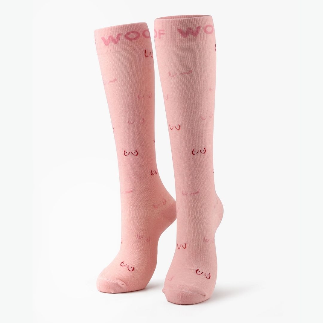 Pair of pink compression socks with line art boobs print standing against a plain background.